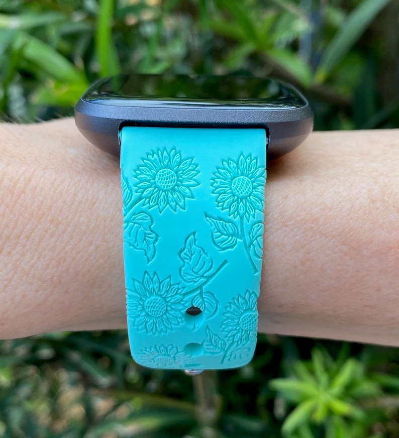 May include: A turquoise blue watch band with a sunflower pattern. The band is made of silicone and has a textured surface.