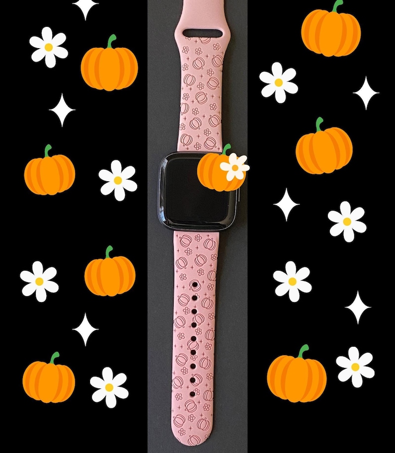 May include: A pink smartwatch band with a pumpkin and flower pattern. The band is attached to a black smartwatch. The background is black with orange pumpkins, white flowers, and white star shapes.