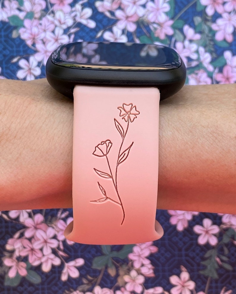 May include: A pink silicone watch band with a delicate floral design. The band is compatible with smartwatches.