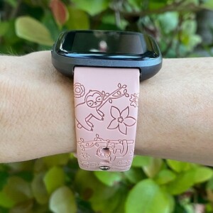 May include: A pink smartwatch band with a sloth design. The band has a black watch face and is worn on a person's wrist.