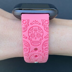 K&ouml;nnte beinhalten: Rosafarbenes Silikon-Armband mit Totenkopf-Design. Das Armband hat ein schwarzes Zifferblatt.