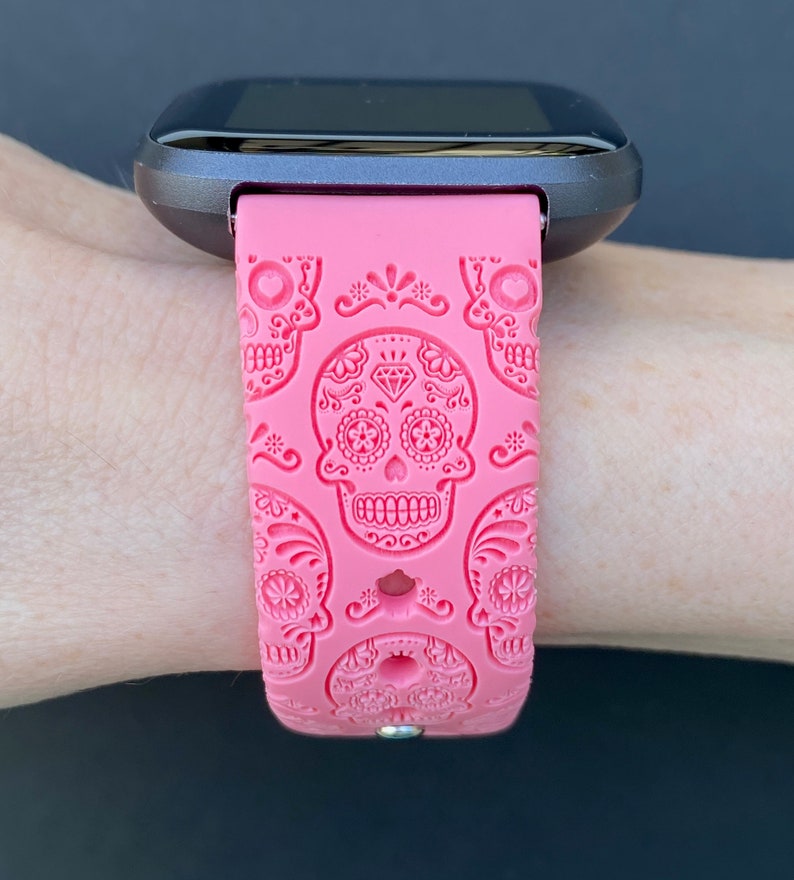 K&ouml;nnte beinhalten: Rosafarbenes Silikon-Armband mit Totenkopf-Design. Das Armband hat ein schwarzes Zifferblatt.