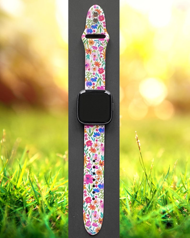 Pu&ograve; includere: Cinturino per smartwatch con motivo floreale e schermo nero. Il cinturino presenta uno sfondo bianco e un motivo colorato di fiori rosa, arancioni, blu e verdi. Il cinturino &egrave; realizzato in materiale flessibile e presenta diversi fori di regolazione.