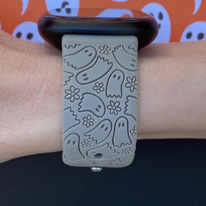 May include: A gray silicone watch band with a ghost pattern. The band is on a person's wrist.