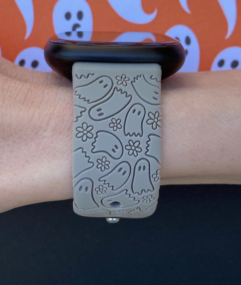 May include: A gray silicone watch band with a ghost pattern. The band is on a person's wrist.