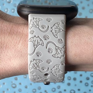 May include: A gray silicone watch band with a pattern of manta rays and seashells. The band is designed for a smartwatch.