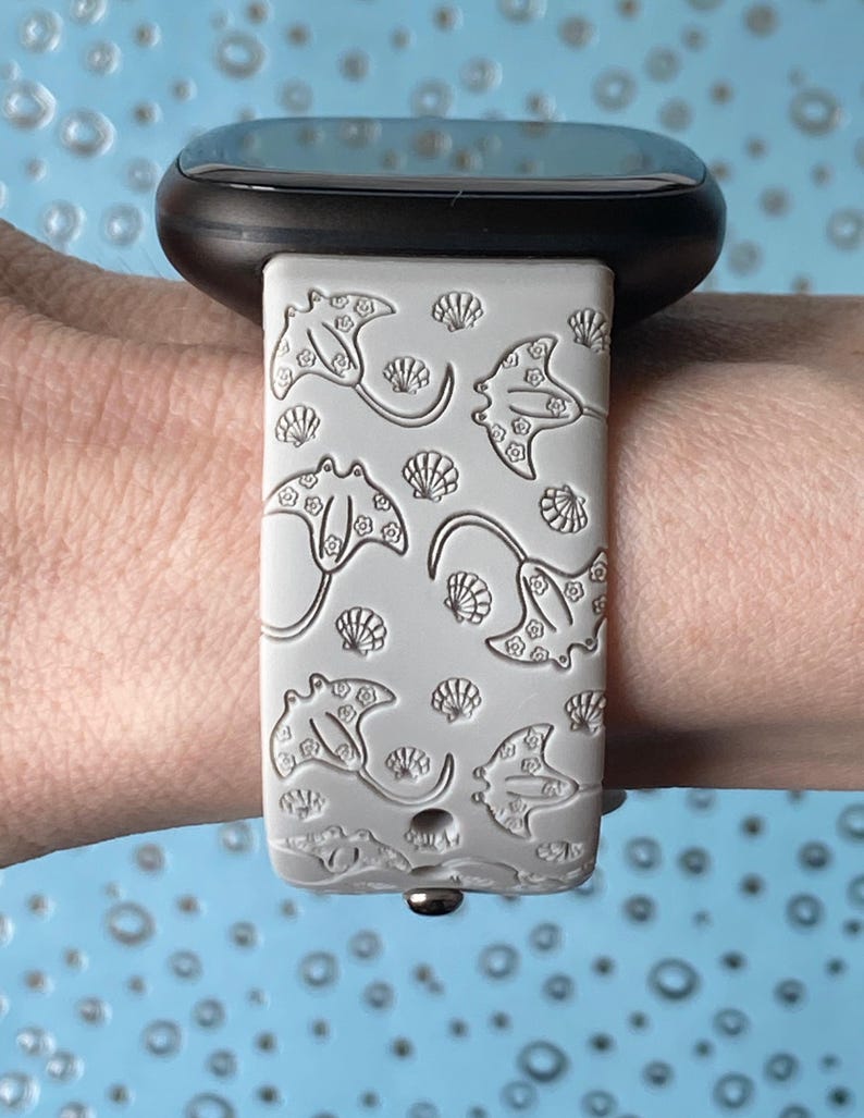 May include: A gray silicone watch band with a pattern of manta rays and seashells. The band is designed for a smartwatch.