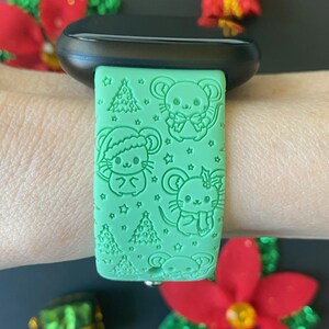 May include: A green silicone watch band with a Christmas theme. The band features a repeating pattern of mice wearing Santa hats, Christmas trees, and stars.