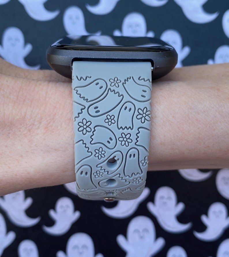 Puede incluir: Una correa de reloj de silicona gris con un patr&oacute;n de fantasmas blancos y flores. La correa est&aacute; dise&ntilde;ada para un reloj inteligente con una cara cuadrada.