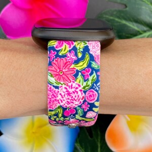 Pu&ograve; includere: Uno smartwatch nero con un cinturino a fantasia floreale. Il cinturino &egrave; rosa, verde e blu con una variet&agrave; di fiori.