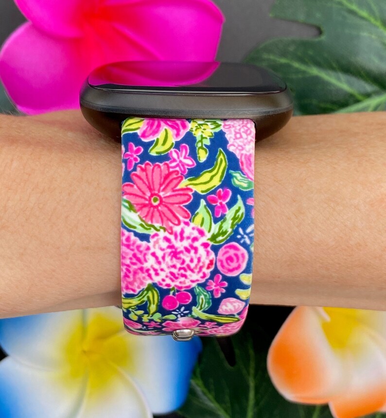 Pu&ograve; includere: Uno smartwatch nero con un cinturino a fantasia floreale. Il cinturino &egrave; rosa, verde e blu con una variet&agrave; di fiori.