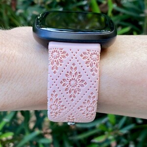Puede incluir: Una banda de reloj inteligente de color rosa con un patr&oacute;n floral. La banda est&aacute; hecha de silicona y tiene una superficie texturizada.