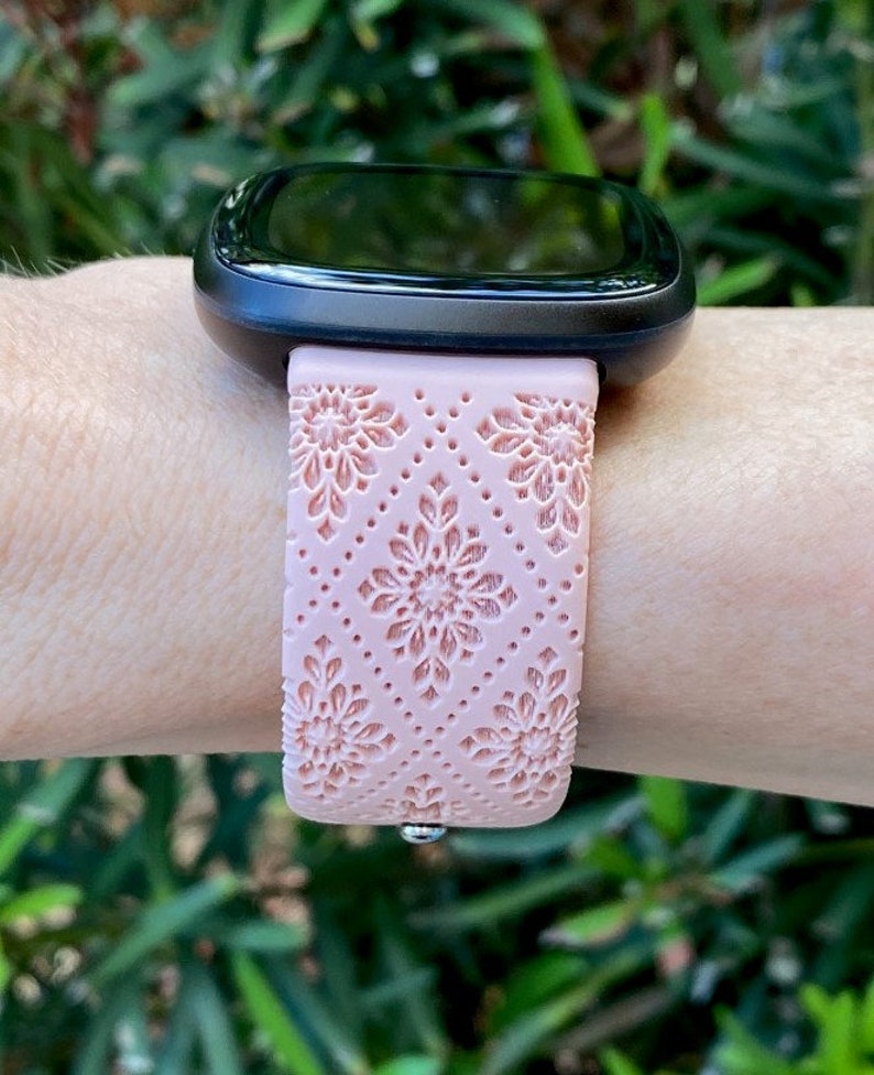 Puede incluir: Una banda de reloj inteligente de color rosa con un patr&oacute;n floral. La banda est&aacute; hecha de silicona y tiene una superficie texturizada.