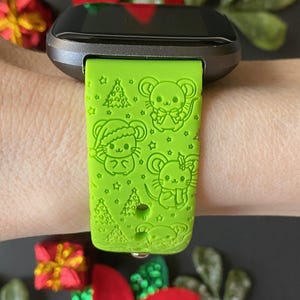 May include: A green smartwatch band with a Christmas-themed design featuring cartoon mice and Christmas trees.