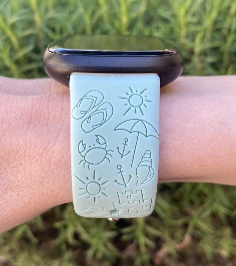 May include: A light green watch band with a beach-themed design. The band features a variety of icons, including flip-flops, a sun, an umbrella, a crab, an anchor, a seashell, and a sandcastle.