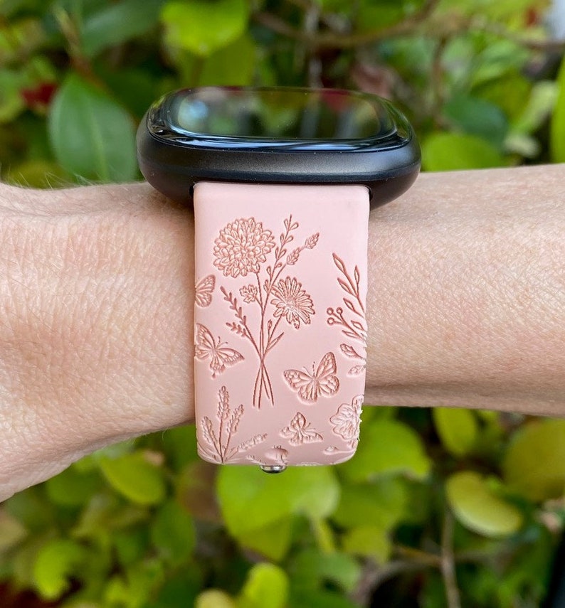 May include: A pink silicone watch band with a floral and butterfly design. The band is compatible with smartwatches.