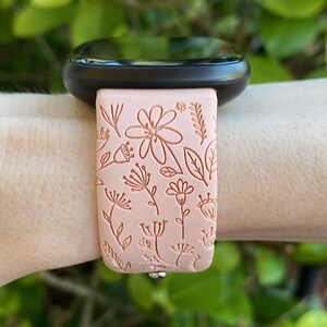 May include: A pink silicone watch band with a floral pattern. The band is designed for a smartwatch and has a silver buckle.