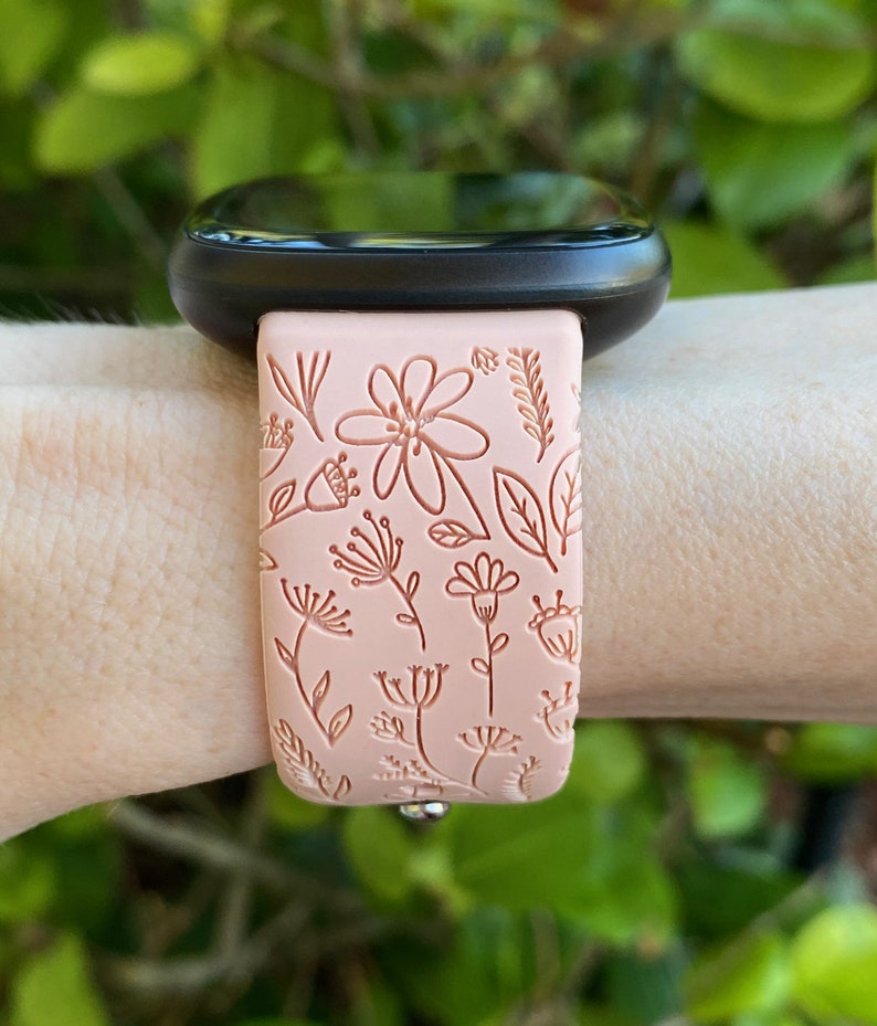 May include: A pink silicone watch band with a floral pattern. The band is designed for a smartwatch and has a silver buckle.