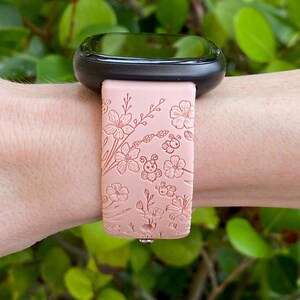 May include: A pink silicone watch band with a floral and bee design. The band is shown on a person's wrist.