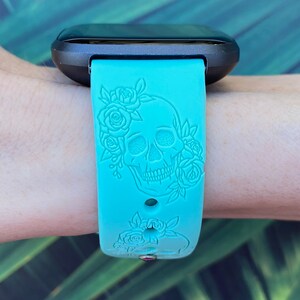 Op de afbeelding: Een turquoise blauwe siliconen horlogeband met een schedel- en rozenontwerp. De band is gegraveerd met een gedetailleerd schedel- en bloemenpatroon.
