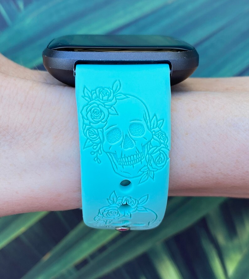 Op de afbeelding: Een turquoise blauwe siliconen horlogeband met een schedel- en rozenontwerp. De band is gegraveerd met een gedetailleerd schedel- en bloemenpatroon.