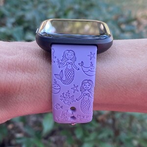 May include: Purple silicone watch band with a mermaid and sea life design. The band has a black watch face.