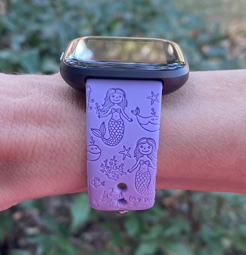 May include: Purple silicone watch band with a mermaid and sea life design. The band has a black watch face.