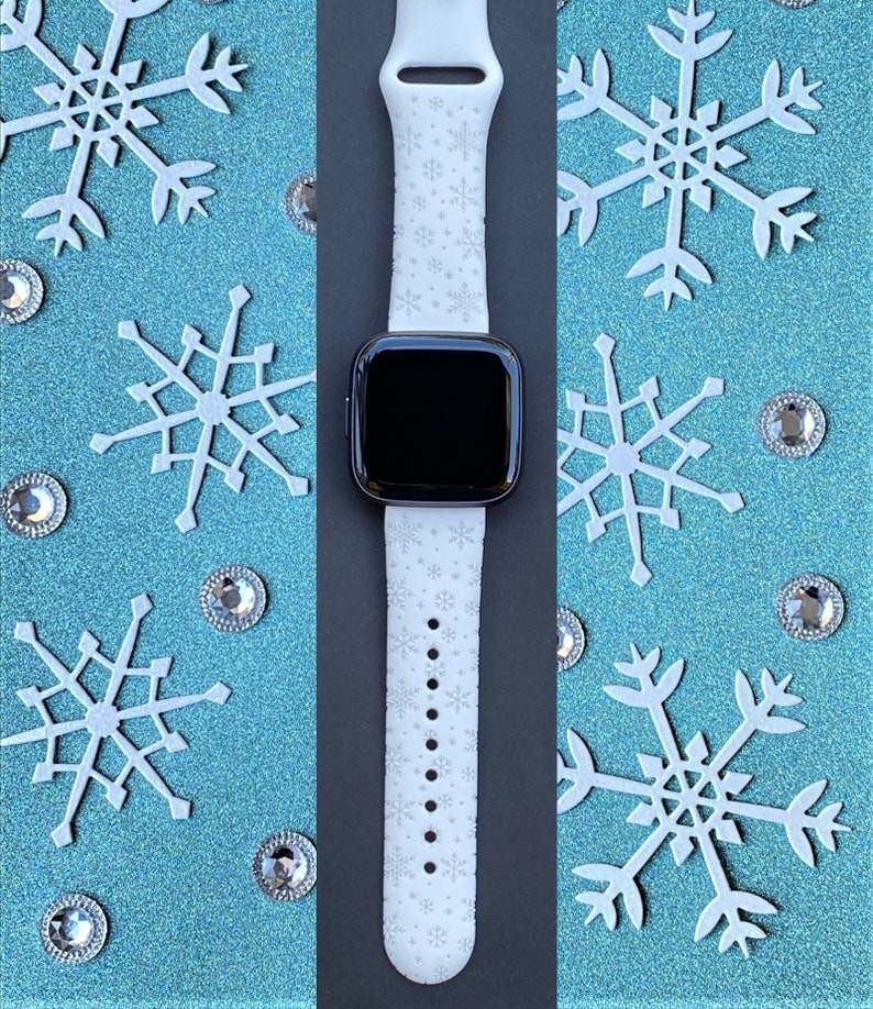 K&ouml;nnte beinhalten: Wei&szlig;es Smartwatch-Armband mit Schneeflockenmuster. Das Armband ist aus Silikon und hat ein schwarzes Zifferblatt.