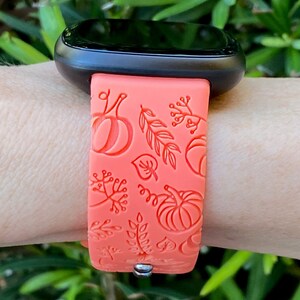 May include: A coral orange silicone watch band with a fall-themed design featuring pumpkins and leaves.
