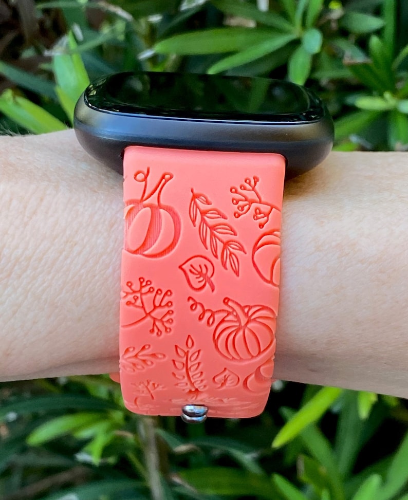 May include: A coral orange silicone watch band with a fall-themed design featuring pumpkins and leaves.
