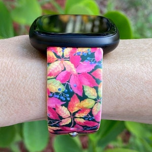 May include: A black smartwatch with a colorful floral band. The band features a pink, yellow, and green floral pattern with dark green leaves and small blue berries.