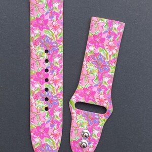 K&ouml;nnte beinhalten: Ein rosafarbenes und wei&szlig;es Armband mit Blumenmuster f&uuml;r die Apple Watch mit silbernen Metallschlie&szlig;en.
