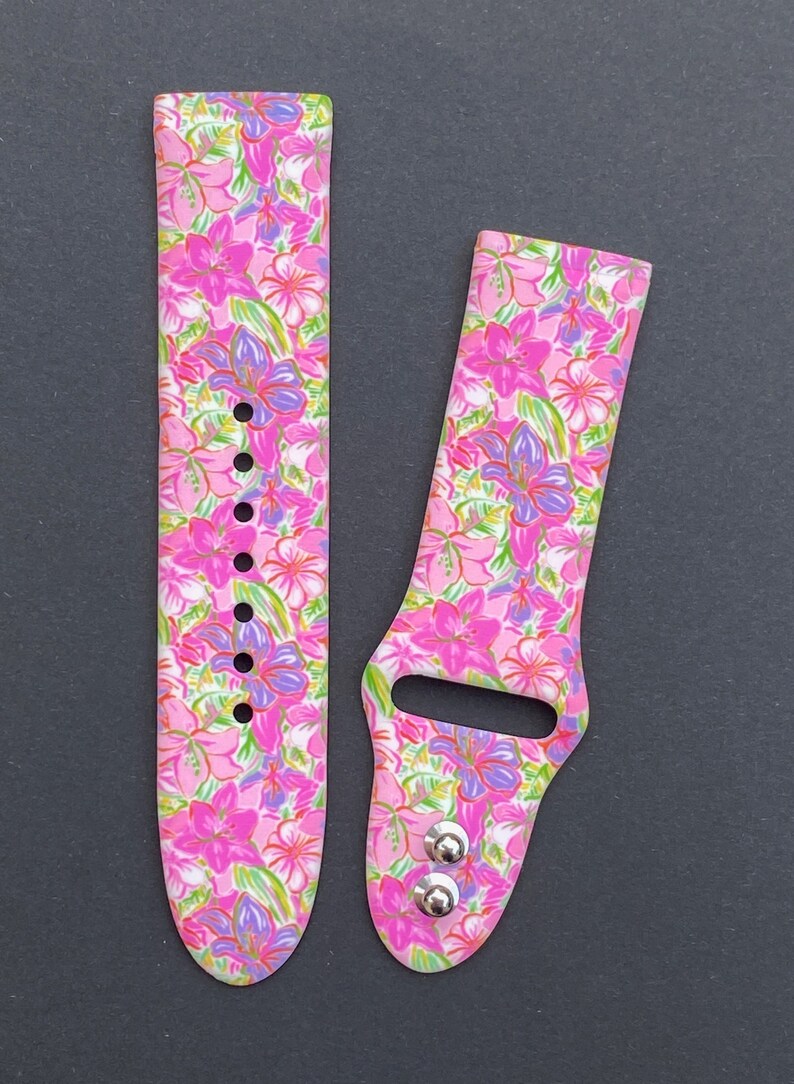 K&ouml;nnte beinhalten: Ein rosafarbenes und wei&szlig;es Armband mit Blumenmuster f&uuml;r die Apple Watch mit silbernen Metallschlie&szlig;en.