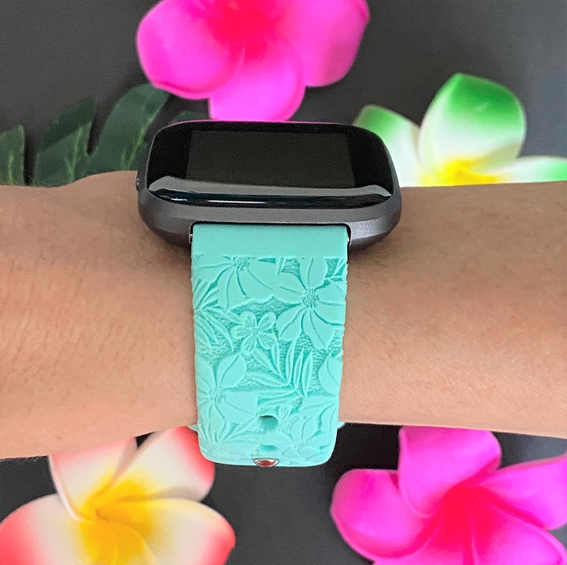 May include: A teal blue fitness tracker band with a floral pattern. The band is made of silicone and has a black buckle.