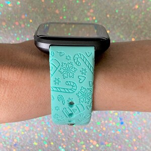 May include: A light blue smartwatch band with a Christmas-themed design featuring snowflakes, candy canes and hearts.