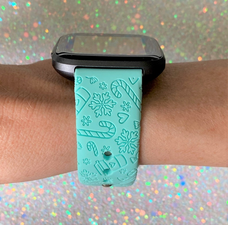 May include: A light blue smartwatch band with a Christmas-themed design featuring snowflakes, candy canes and hearts.