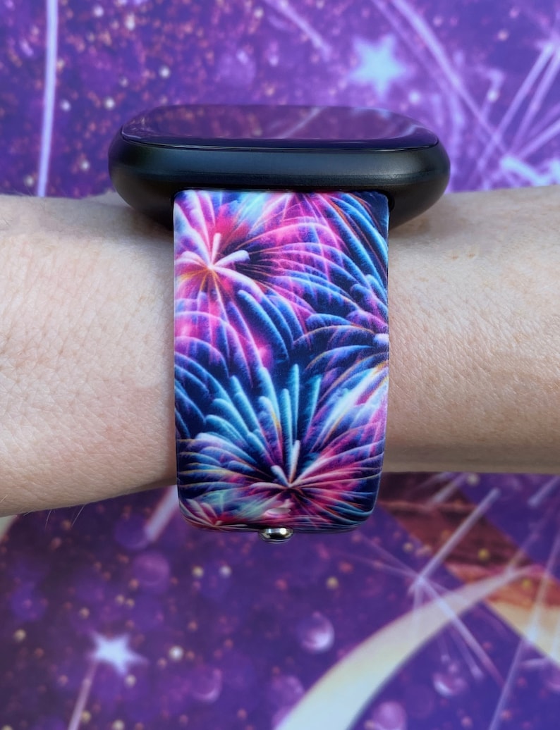 May include: A black smartwatch with a colorful firework print band. The band is made of silicone and has a vibrant design with pink, blue, and purple fireworks.