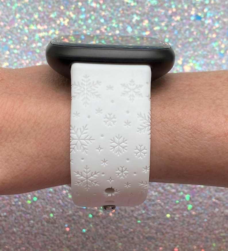 Pu&ograve; includere: Cinturino bianco per smartwatch con motivo a fiocco di neve. Il cinturino &egrave; in silicone e ha una fibbia in metallo nero.