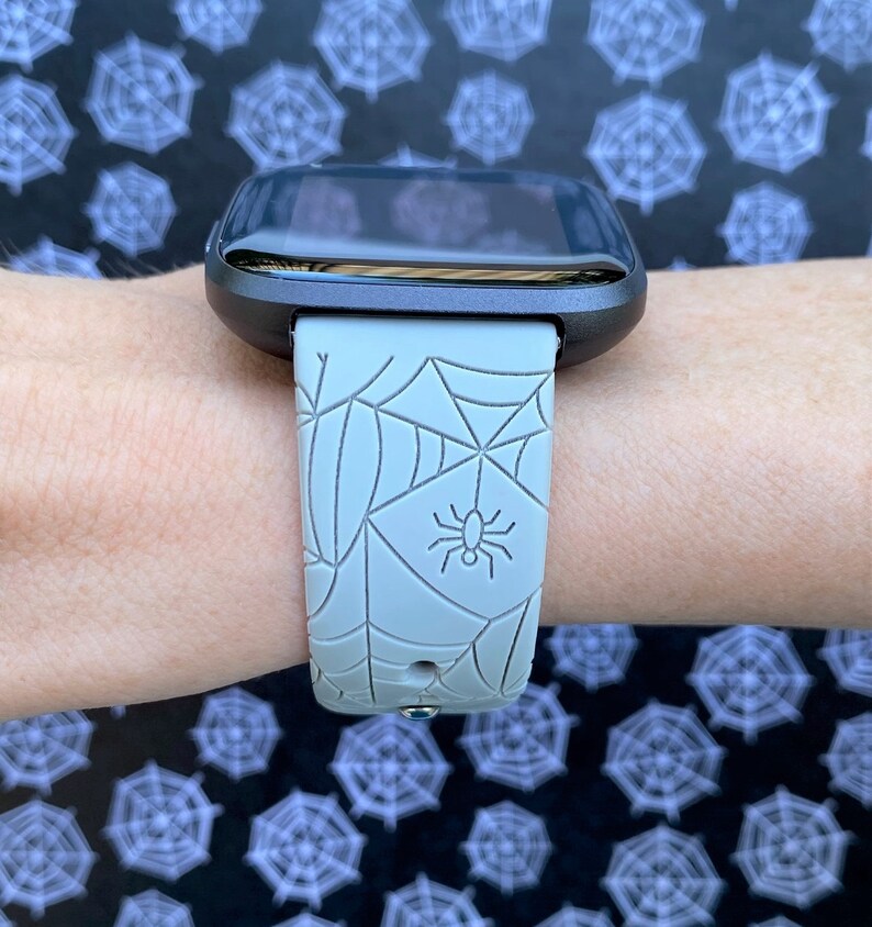 May include: A gray smartwatch with a spiderweb and spider design on the band.