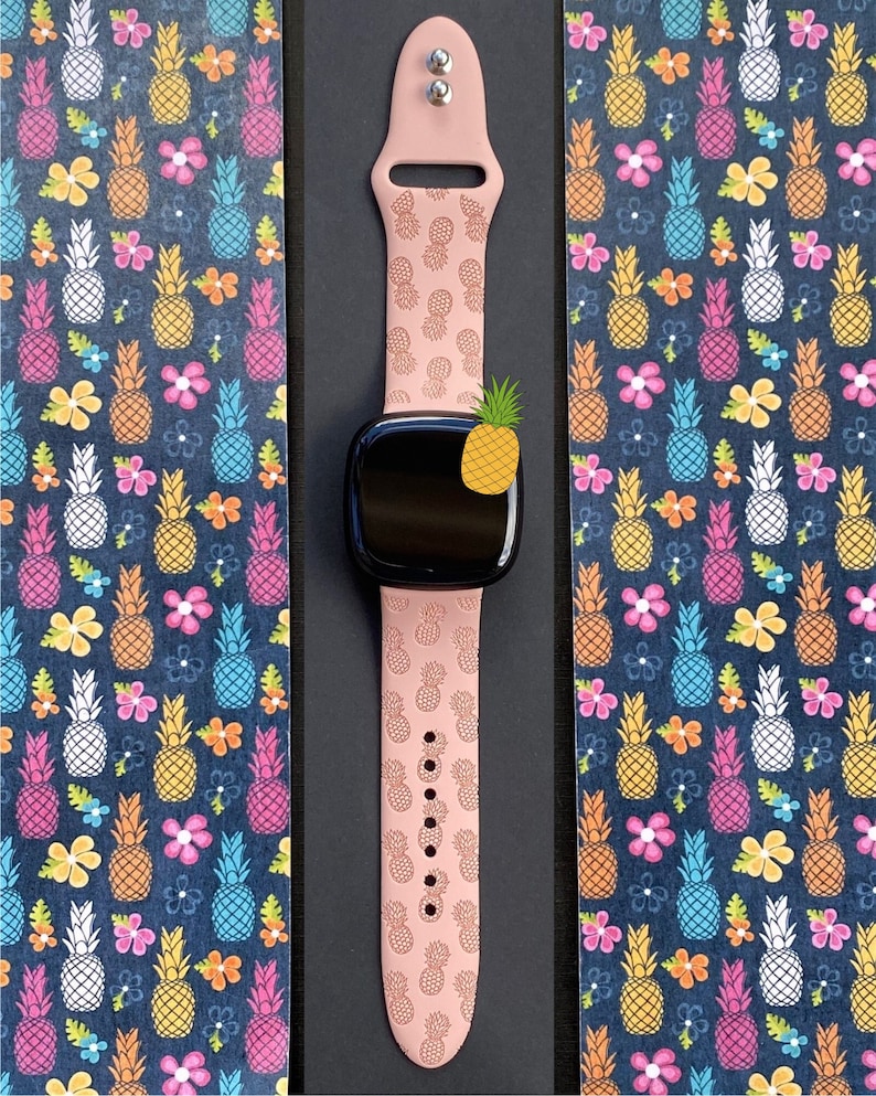 May include: A pink silicone watch band with a pineapple pattern. The band is designed for a smartwatch and has a black watch face.