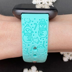 May include: A turquoise blue smartwatch band with a winter-themed design featuring snowmen, candy canes, and hot chocolate.