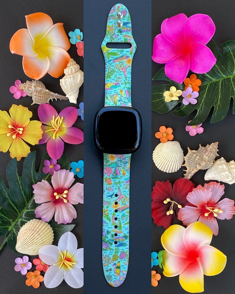 K&ouml;nnte beinhalten: Ein blaues und wei&szlig;es Apple Watch Armband mit einem schwarzen Zifferblatt. Das Armband hat einen tropischen Druck mit Palmen, Segelbooten und Fischen. Die Uhr ist von bunten Blumen und Muscheln umgeben.