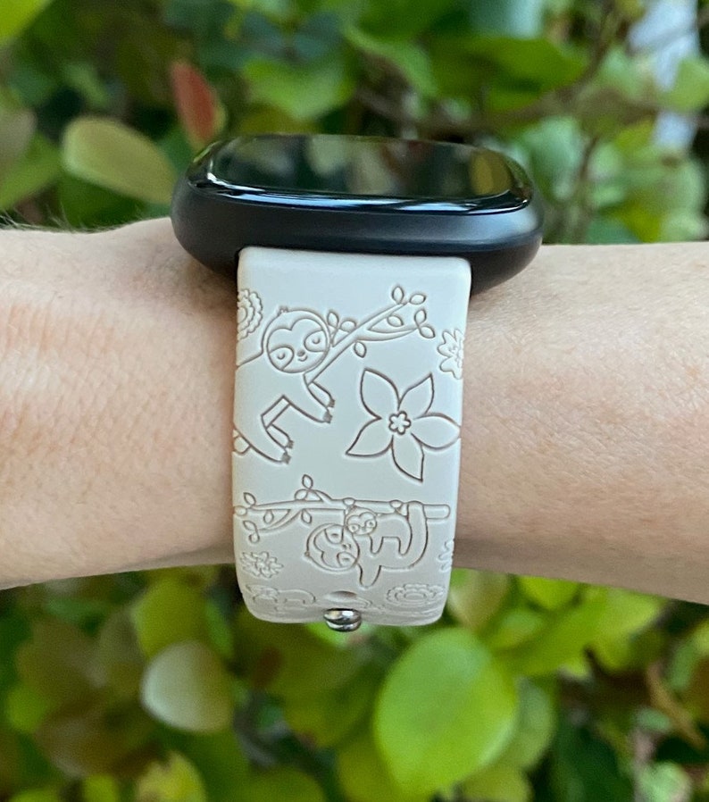 May include: A white smartwatch band with a black watch face. The band has a pattern of sloths and flowers.