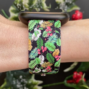 May include: A black smartwatch with a green, red and gold patterned band featuring a holly and berry design.