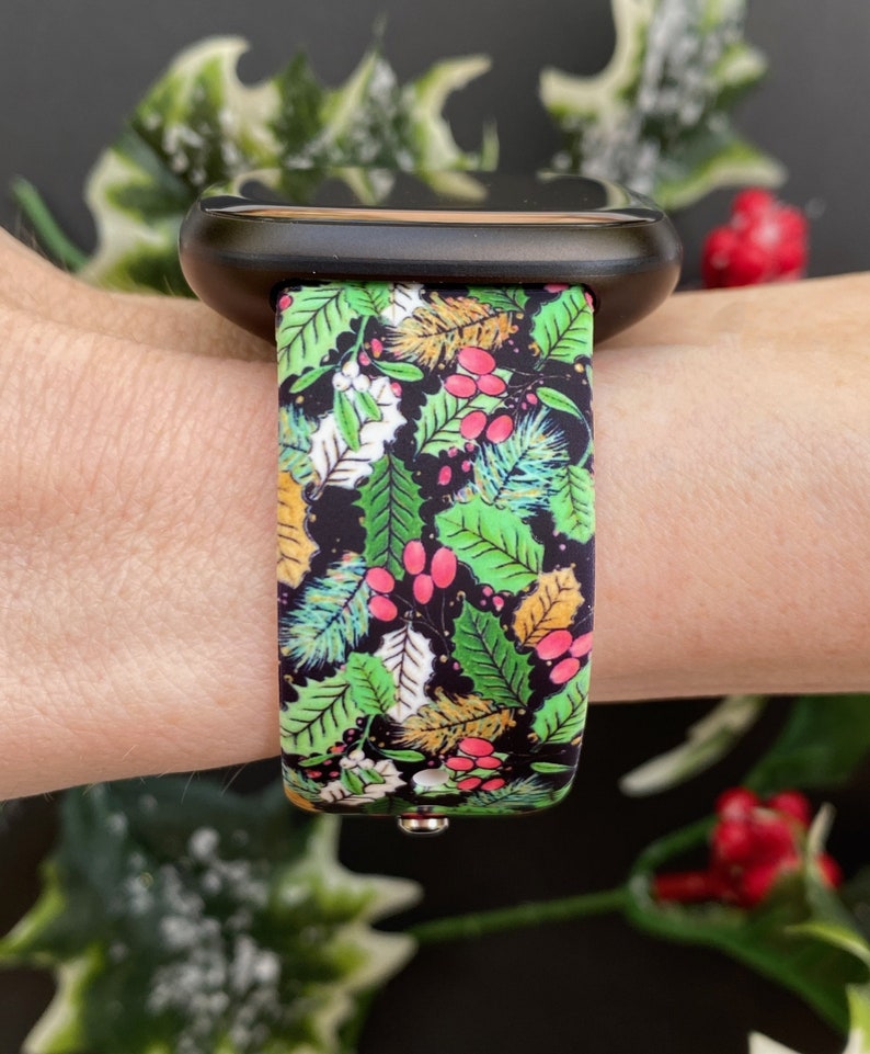 May include: A black smartwatch with a green, red and gold patterned band featuring a holly and berry design.