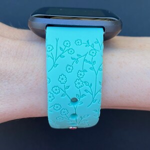 May include: A turquoise smartwatch band with a floral pattern. The band is made of silicone and has a textured surface.