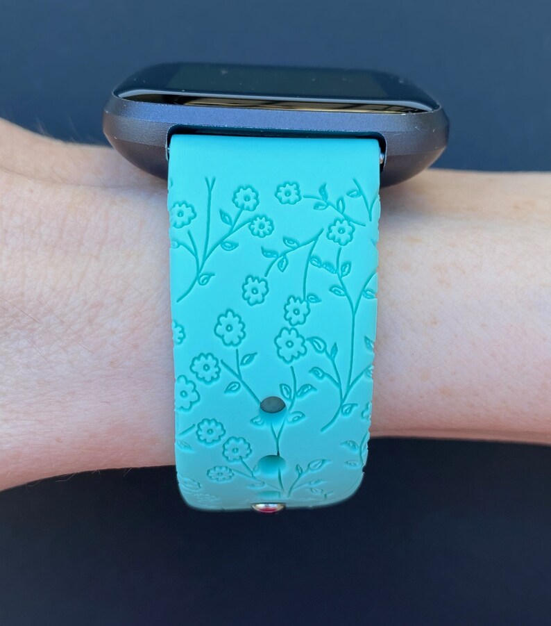 May include: A turquoise smartwatch band with a floral pattern. The band is made of silicone and has a textured surface.