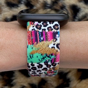 K&ouml;nnte beinhalten: Ein farbenfrohes Armband mit Leopardenmuster, rosa, gr&uuml;nen und goldenen Akzenten. Das Armband ist aus Silikon und hat einen wei&szlig;en Hintergrund.