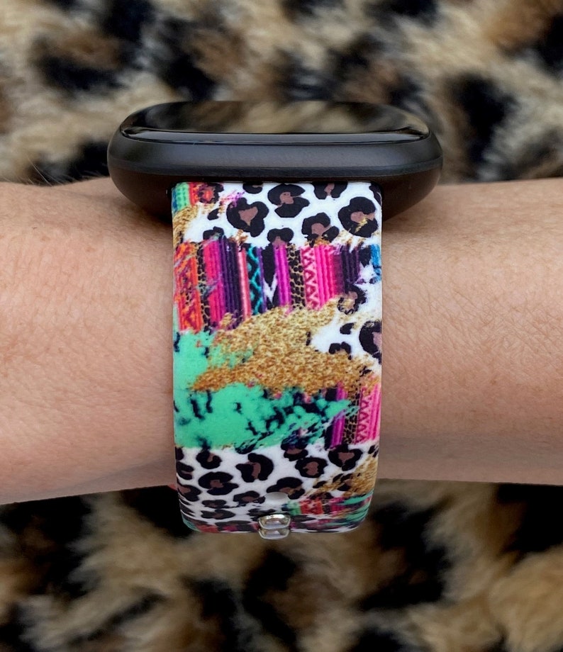 K&ouml;nnte beinhalten: Ein farbenfrohes Armband mit Leopardenmuster, rosa, gr&uuml;nen und goldenen Akzenten. Das Armband ist aus Silikon und hat einen wei&szlig;en Hintergrund.