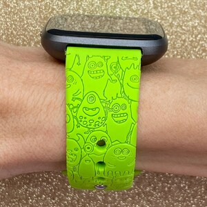 Puede incluir: Una correa de reloj de silicona verde con un estampado de monstruo de dibujos animados. La correa est&aacute; dise&ntilde;ada para un reloj inteligente con una esfera negra.